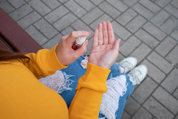 Młoda dziewczyna w żółtym swetrze dezynfekuje ręce środkiem dezynfekującym. - Zdjęcie, obraz