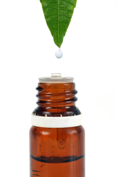 Concepto de aromaterapia con una gota cayendo de una hoja en una botella de aceite esencial sobre un fondo blanco
 - Foto, imagen