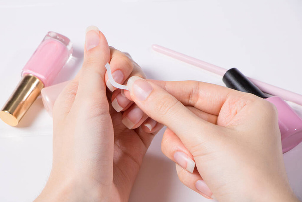 Manicure. Een vrouw lijmt stickers op haar nagels voor Franse manicure. Het meisje brengt nagellak aan. Nagelsalon, procedure, SPA. Thuis nagelverzorging. Manicure gereedschap. Schoonheid, nagelkunst, Glamour. - Foto, afbeelding