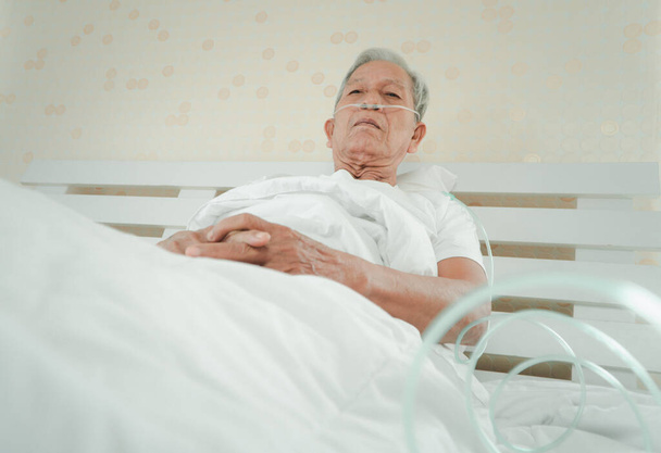 Smutný starší muž ležící na nemocničním lůžku a s nosní dýchací trubicí pro léčbu dýchacích cest. Koncepce zdravotní péče pro seniory, karanténní koronavirus (COVID-19) - Fotografie, Obrázek