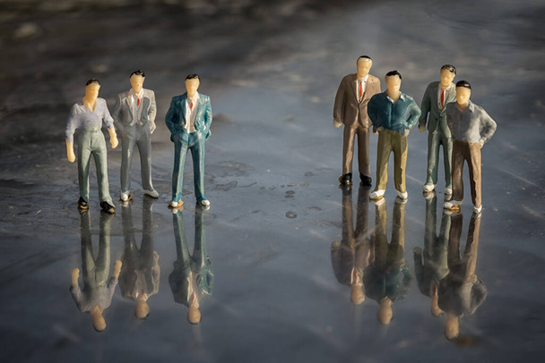 Dos equipos de personas en miniatura empresarios de pie en una superficie reflectante
.  - Foto, Imagen
