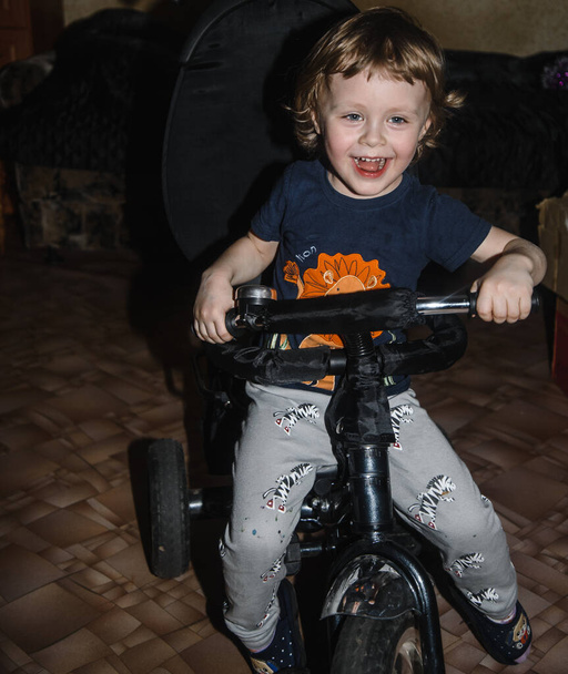 krullend baby jongen rijdt een fiets en lacht - Foto, afbeelding