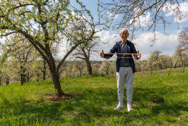 Vecchio uomo europeo che allunga il muscolo nel concetto di allenamento a casa con banda di resistenza
. - Foto, immagini