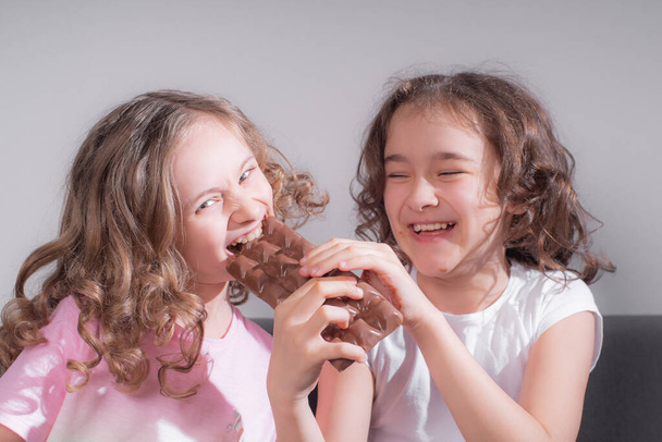 Діти та шоколад. Дві веселі дівчата їдять шоколад на світлому тлі
. - Фото, зображення