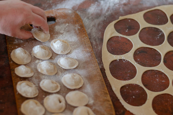 Female hand lays raw homemade dumplings. Serving of dumplings with meat on a wooden cutting board. Homemade food. Focus in the background. - Foto, Bild
