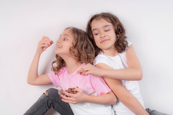 Παιδιά και σοκολάτα.Δύο χαρούμενα κορίτσια τρώνε σοκολάτα σε ελαφρύ φόντο. - Φωτογραφία, εικόνα
