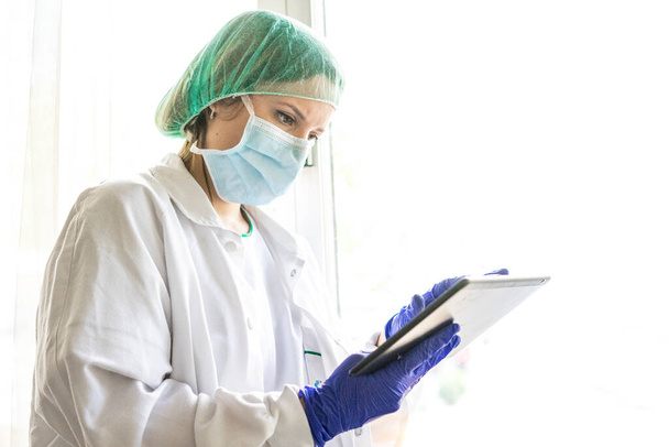 Обрезанный снимок неузнаваемой медсестры с помощью цифрового планшета, стоящей в больнице. whit a mask - Фото, изображение