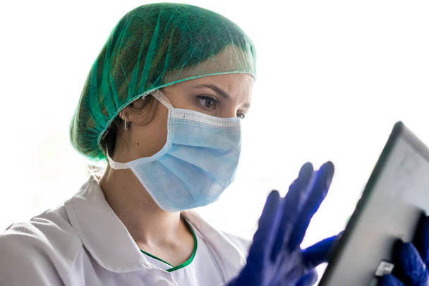 Colpo ritagliato di un'infermiera irriconoscibile che usa una tavoletta digitale mentre si trova in ospedale. con una maschera - Foto, immagini