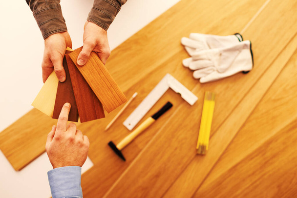 Carpenter showing some wooden baseboard swatches to a customer and choosing a color, flooring installation and work tools on background - Zdjęcie, obraz