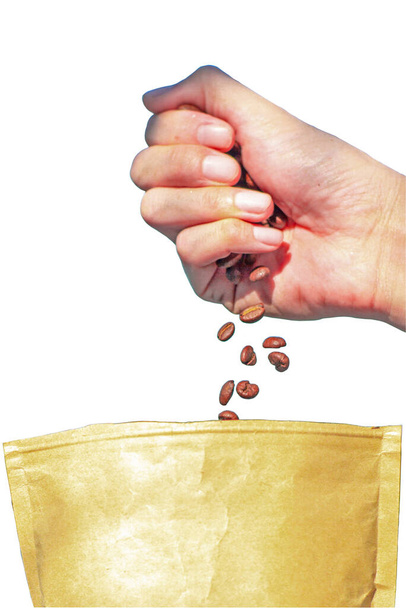 Рука крупным планом выпускает кофейные зерна в бумажный коричневый мешок изолированы на белом фоне
. - Фото, изображение
