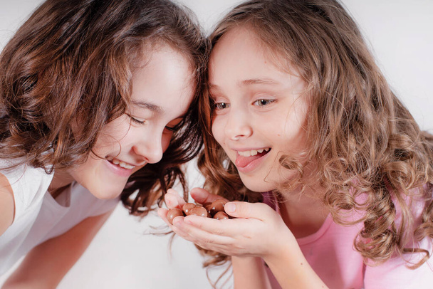 Les enfants et le chocolat.Deux filles gaies mangent du chocolat sur un fond clair. - Photo, image