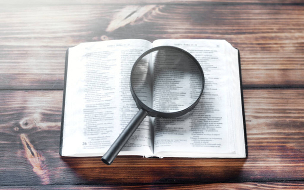 Open bijbel op een houten tafel. Vergrootglas - Foto, afbeelding