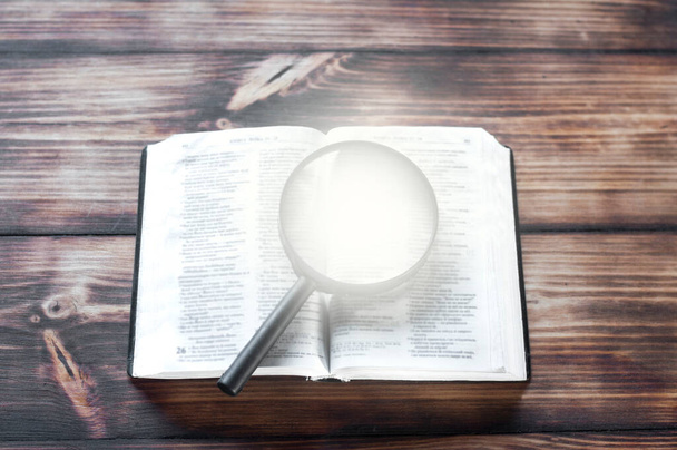 Открыть Библию на деревянном столе. Увеличитель
 - Фото, изображение