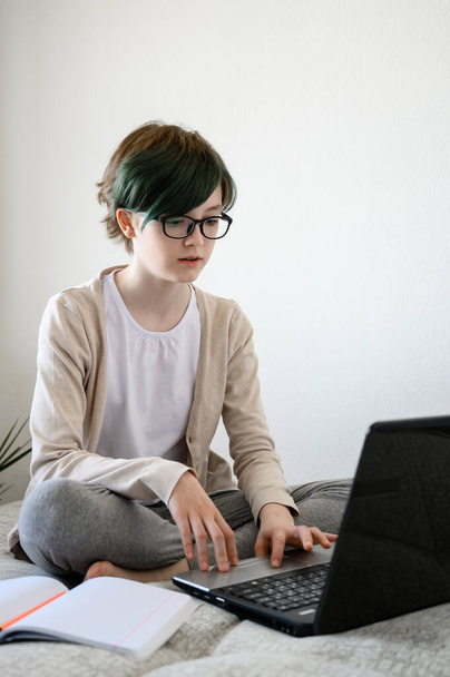 Online onderwijs op afstand. Tiener schoolmeisje studeren thuis, met behulp van laptop. blank meisje zitten op bed en doen school huiswerk. - Foto, afbeelding