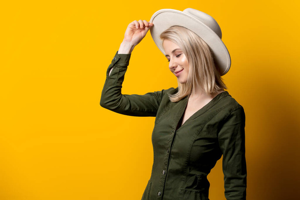 Blondýny žena v klobouku a zelené košili na žlutém pozadí  - Fotografie, Obrázek