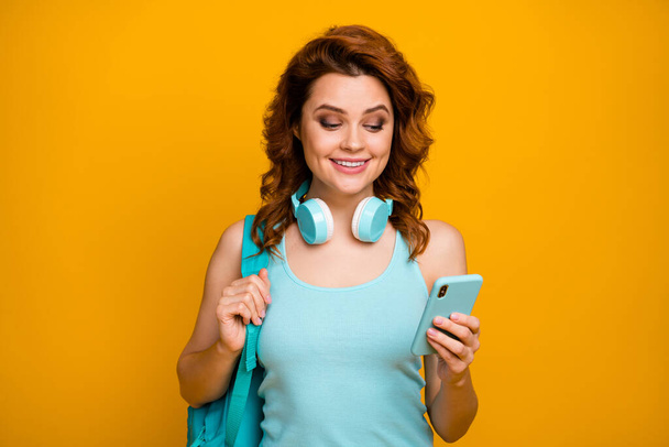 Photo of attractive cheerful student lady hold telephone turn on favorite song listen cool headphones playlist wear backpack casual teal singlet isolated bright yellow color background - Foto, Imagem
