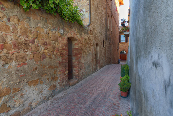Krásná úzká ulice se sluncem a květy v malé magické a staré vesnici Pienza, Val D 'Orcia Toskánsko, Itálie - Fotografie, Obrázek