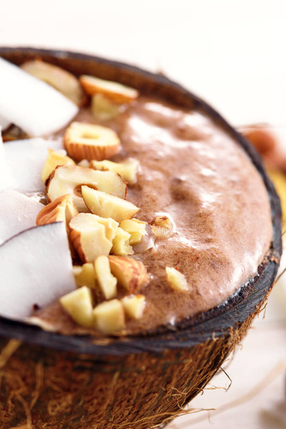 zbliżenie pionowa miska smoothie z mus czekoladowy, orzech laskowy, płatki kokosowe w misce kokosowej, koncepcja lodów czekoladowych, deser ekologiczny - Zdjęcie, obraz