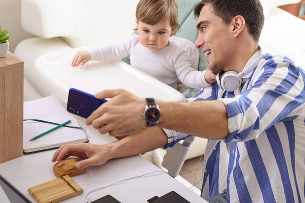 папа фрилансер на рабочем столе делает селфи с ребенком, удаленная работа на дому, концепция отцовства
 - Фото, изображение