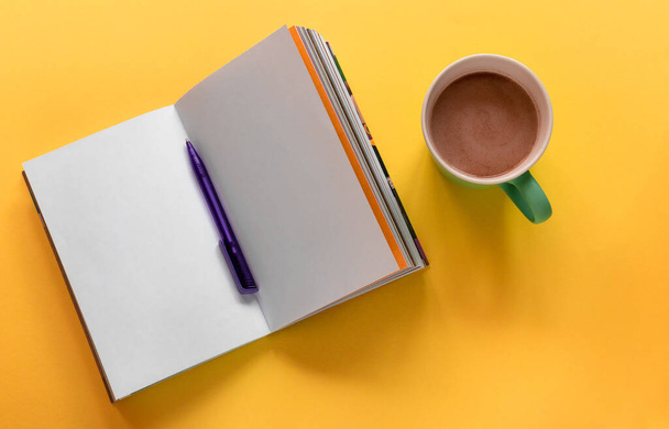 Open notebook/sketchbook with pen and cup of coffee on yellow background. Flat lay design with copy space. Working place concept - Foto, afbeelding