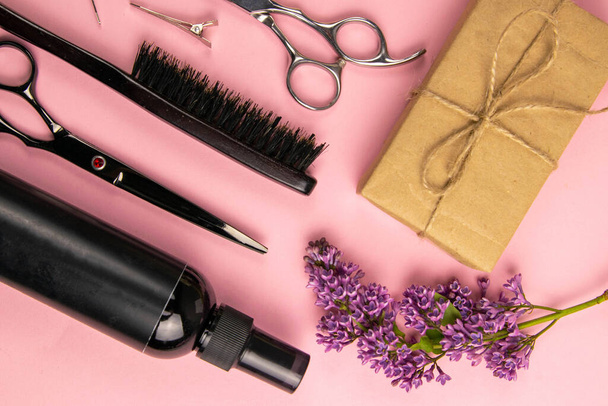 Outils de coiffure - ciseaux, peignes, gel capillaire, épingles à cheveux et fleurs lilas avec café sur fond rose. Concept beauté. Couché plat, vue du dessus
. - Photo, image