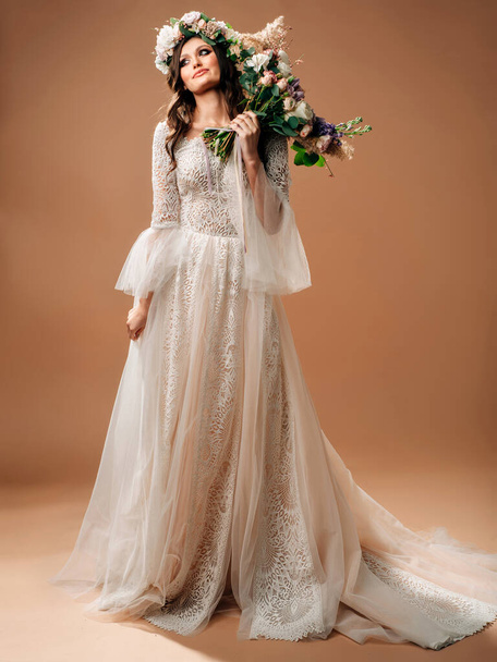 Boho-Hochzeitsstil. Studioporträt der schönen Braut in wunderschönem Brautkleid mit Schleppe hält großen Strauß und floralen Girlanden.  - Foto, Bild