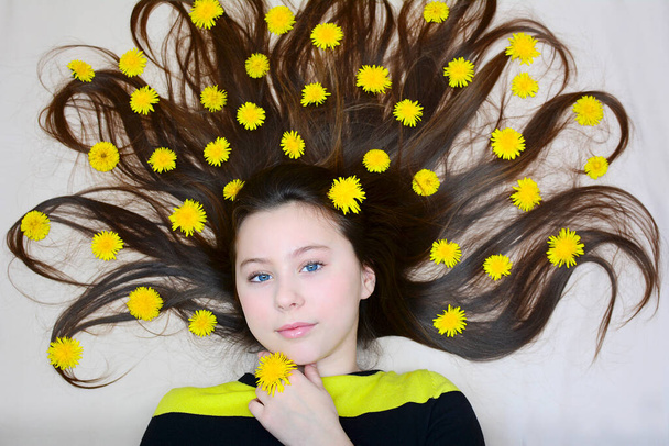 A young girl lies with dandelion flowers in her loose long hair. View from above. Portrait - Φωτογραφία, εικόνα