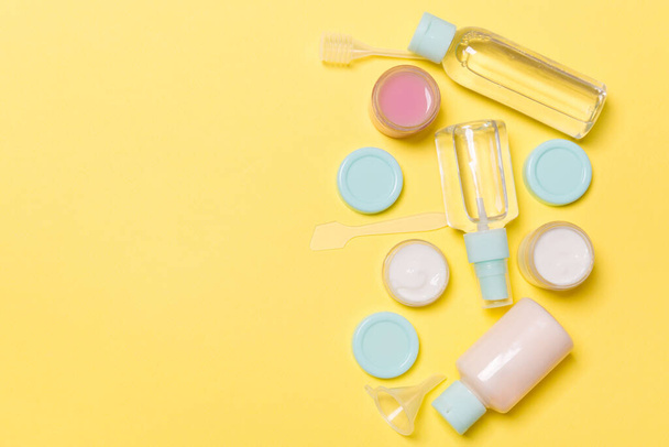 Top view composition of small travelling bottles and jars for cosmetic products on yellow background. Facial skin care concept with copy space for your design. - Фото, зображення