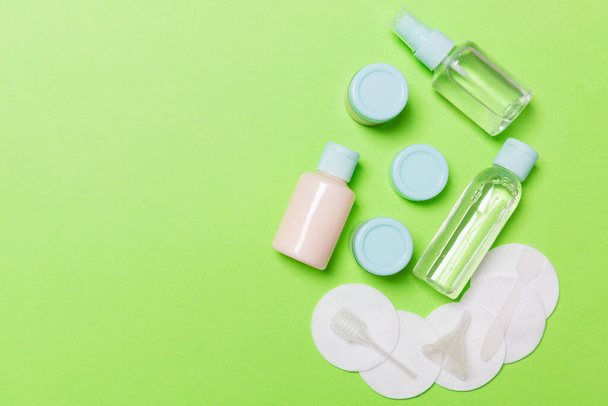 Group of small bottles for travelling on green background. Copy space for your ideas. Flat lay composition of cosmetic products. Top view of cream containers with cotton pads. - Photo, Image