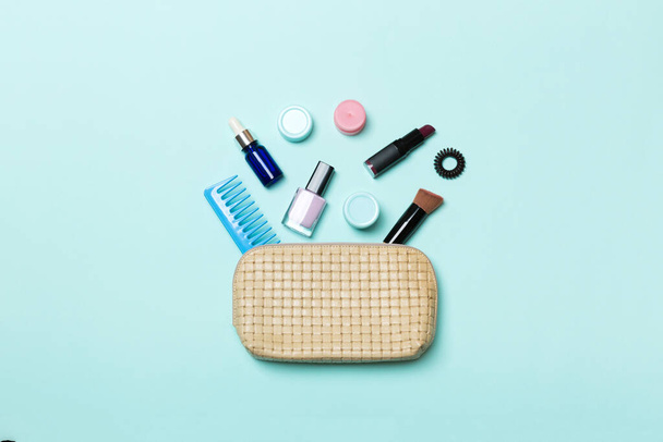 Top view of set of make up and skin care products spilling out of cosmetics bag on blue background. Beauty concept. - Photo, Image