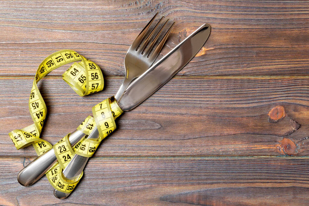 フォークとナイフを交配し、木製の背景にテープを測定するダイエットと健康的な食事の概念。減量のトップビュー. - 写真・画像