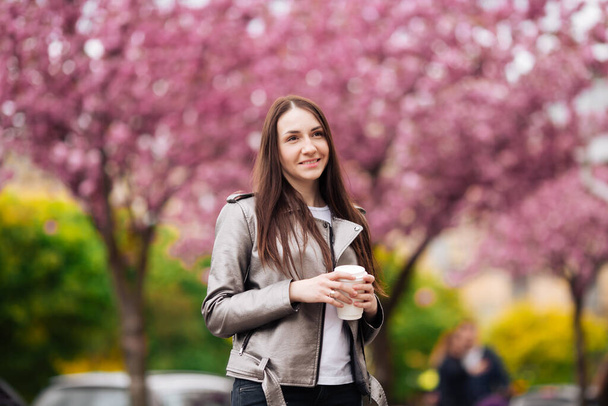 Woman in good mood posing with cup of coffee against sakura tree - Fotó, kép