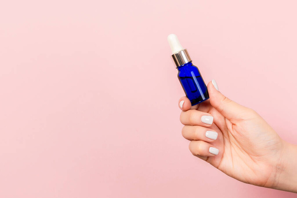 Weibliche Hand hält eine Flasche Kosmetikprodukt auf rosa Hintergrund mit leerem Raum für Ihr Design. - Foto, Bild