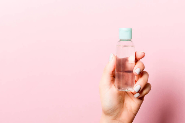 A bottle of cosmetic product in a female hand at pink background with copy space. - Zdjęcie, obraz