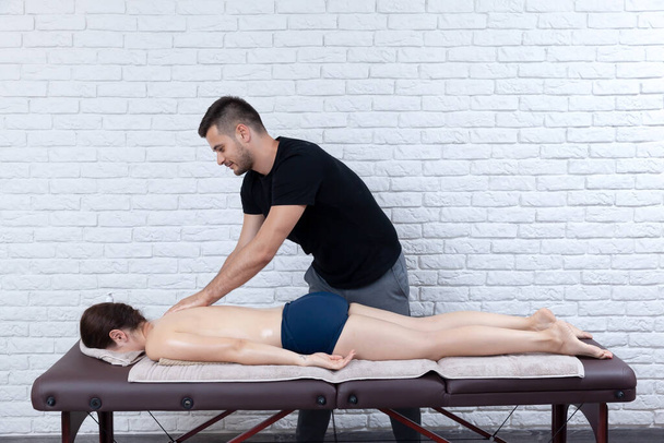 Jonge vrouw krijgen massage seesion thuis door een fysiotherapeut. - Foto, afbeelding