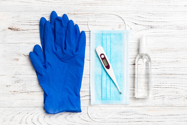 Top view of surgical mask, latex gloves, alcohol hand sanitizer and digital thermometer on wooden background with copy space. Protective medical equipment concept. - Photo, Image