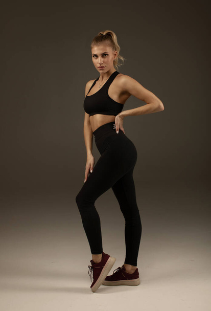 Happy young woman in sports clothing smiling. Muscular fitness model on grey background looking away at copy space. Trained body. - Zdjęcie, obraz