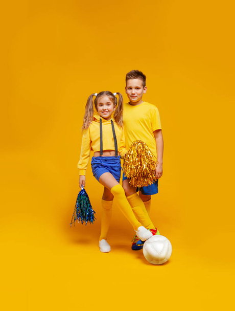 Μια μαζορέτα και ένας ποδοσφαιριστής με την ίδια στολή στέκονται, κρατώντας την μπάλα με το πόδι του. Κοριτσίστικα πομπούς - Φωτογραφία, εικόνα