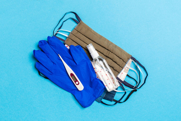 アルコールハンドサニタイザー、ラテックス手袋、デジタル温度計、青の背景に手作りの再利用可能なマスクのトップビュー。コピースペースとウイルス対策機器の概念. - 写真・画像