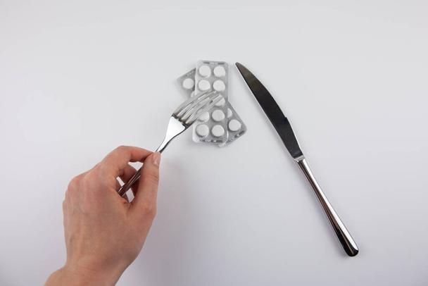 Iron fork and knife with pills on a white background. Use of medications. Care of health. Excessive use of medications during treatment. Eating pills. - Foto, Imagem