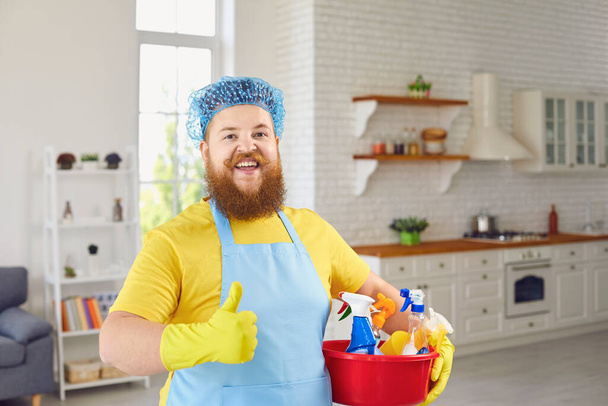 Funny fat man with a beard in an apron cleans the room in the house. - Photo, image