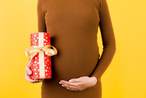 Zugeschnittenes Bild einer schwangeren Frau in weißer Unterwäsche, die eine Geschenkbox hält und ihren Bauch vor blauem Hintergrund berührt. Erwartung eines kleinen Mädchens. Kopierraum. - Foto, Bild