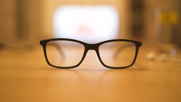 Schwarze Brillengestelle auf dem Küchentisch. TV-Bildschirm durch Brille gesehen - Filmmaterial, Video