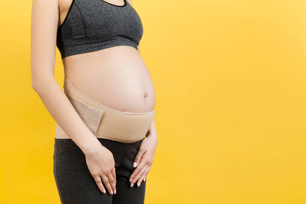 Крупним планом вагітна жінка з підтримуючою пов'язкою проти беккача на жовтому тлі з копіювальним простором. Концепція ортопедичного поясу підтримки живота
. - Фото, зображення
