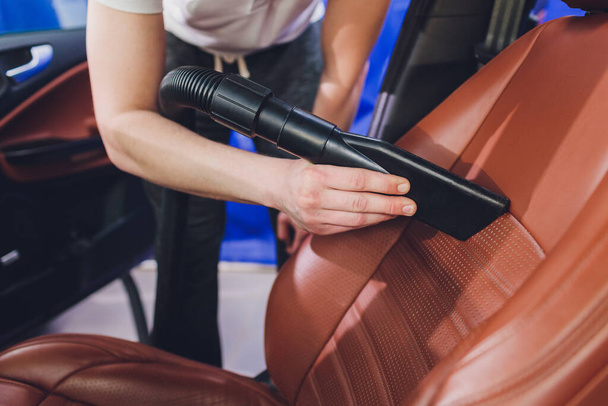 vehicle interior vacuum cleaning. Detail shot of an industrial vacuum cleaner cleaning a car seat. - Zdjęcie, obraz