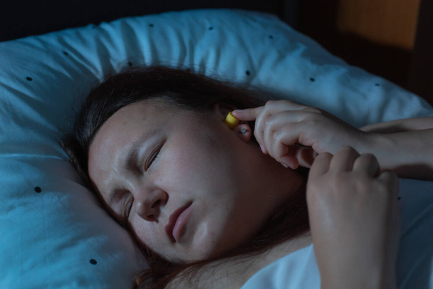 Молода жінка кладе вушні пробки в вуха для зменшення шуму перед сном, безсоння
 - Фото, зображення