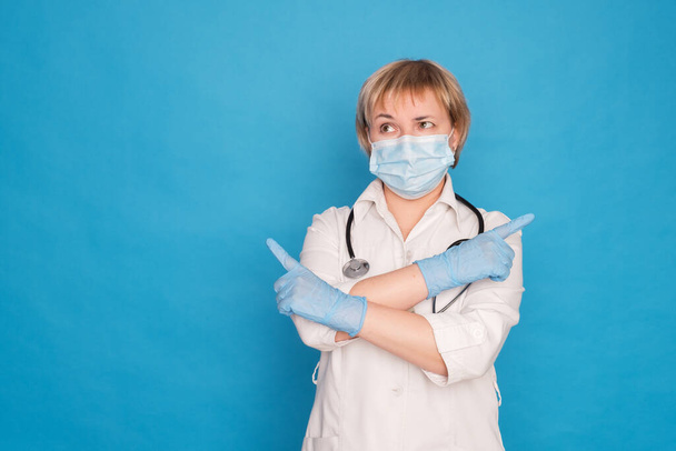 Eldery caucasian doctor lady in white coat and with stethoscope on blue background. Emotional portraits: she points her fingers. - Фото, зображення