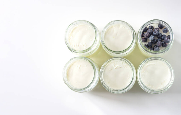 Homemade milk yogurt in glass jars with blueberries on a white table. Cooking at home during quarantine. Top view, copy space - Valokuva, kuva