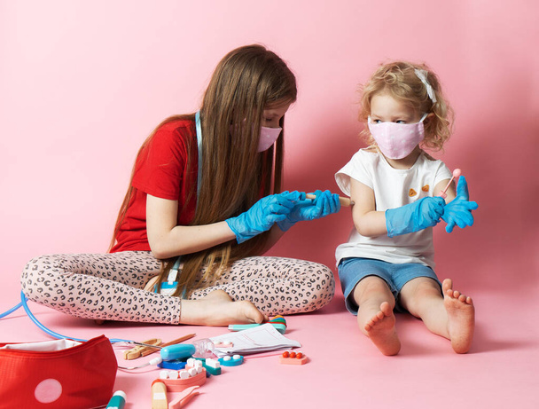 Personal protective equipment: two girls in medical masks and gloves play doctor and use a medical kit from toys. - Zdjęcie, obraz