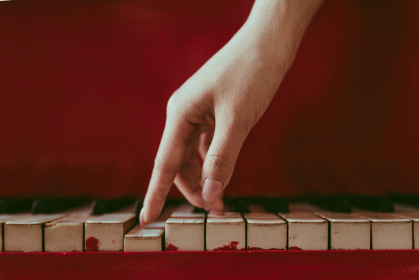 a close-up of a side view with female hand with pink manicure playing the piano. An old red piano with black and white keys. A palm above the keyboard. Graceful fingers of composer or musician - Foto, Imagen